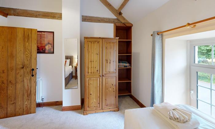 Twin bedroom with rustic wood wardrobe, ceiling beams, and garden views from two windows.